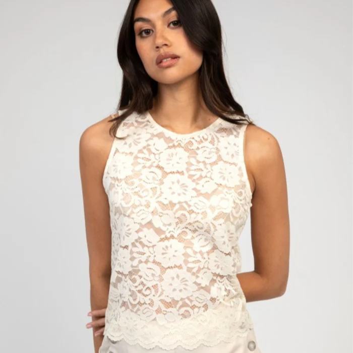 Woman wearing a white lace top and white pants against a gray background