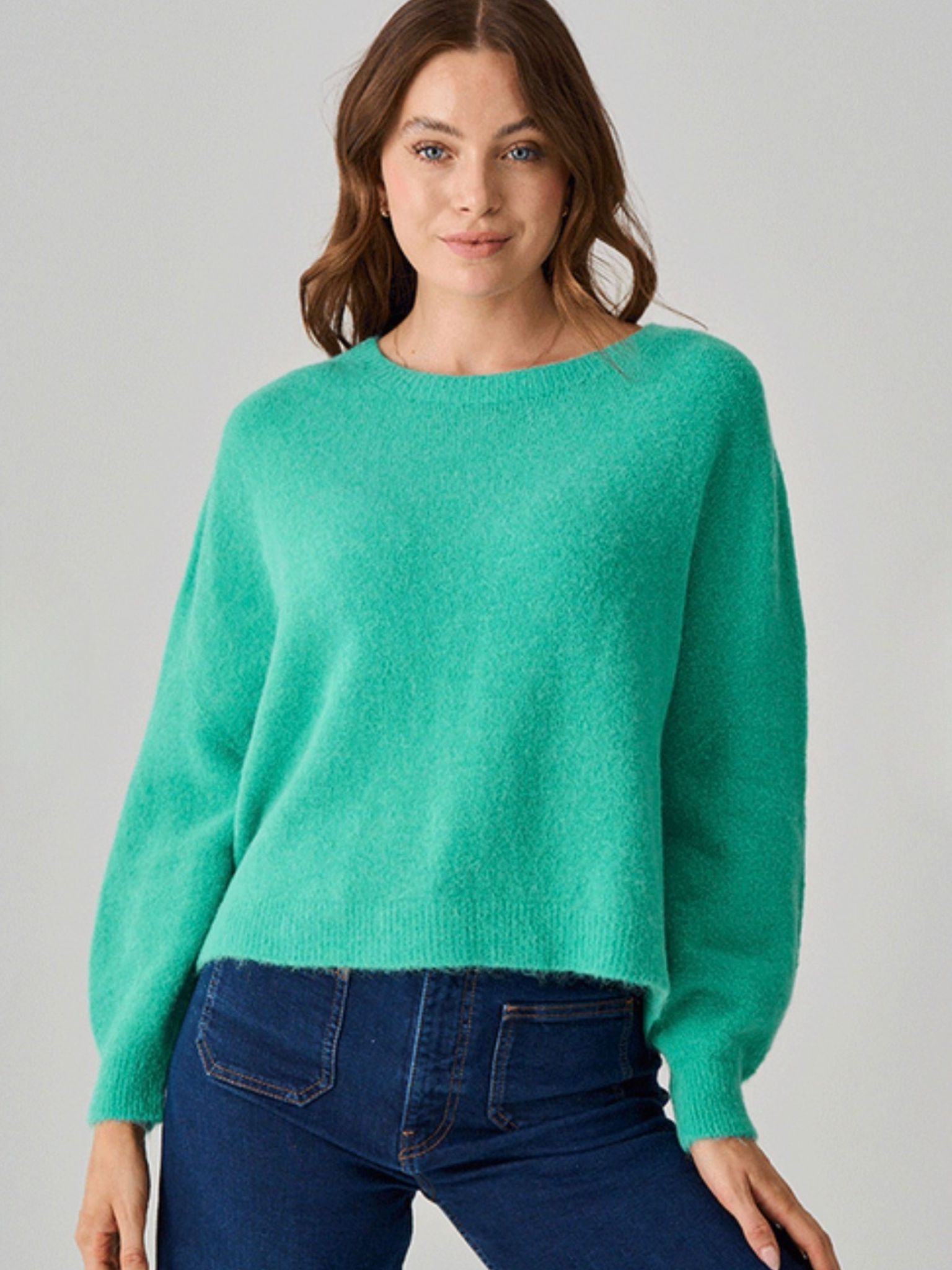 Woman wearing a green sweater and blue jeans on a gray background