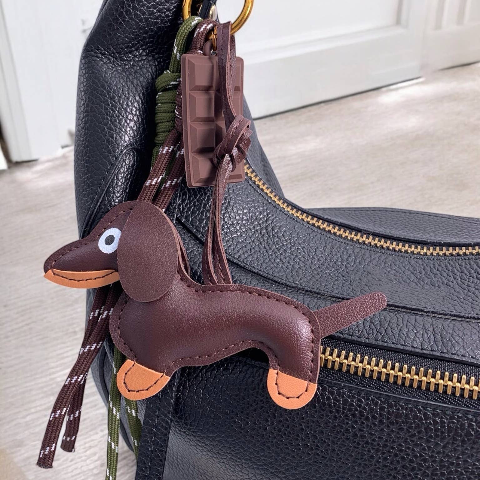 Brown dachshund-shaped keychain attached to a black leather bag.