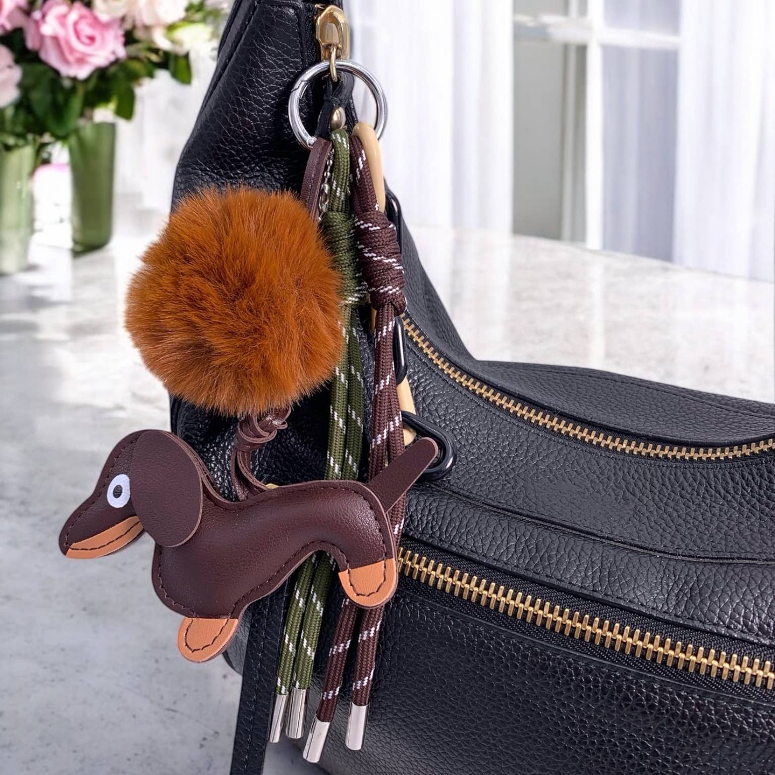 Black handbag with a dachshund keychain and a fluffy pom-pom attached