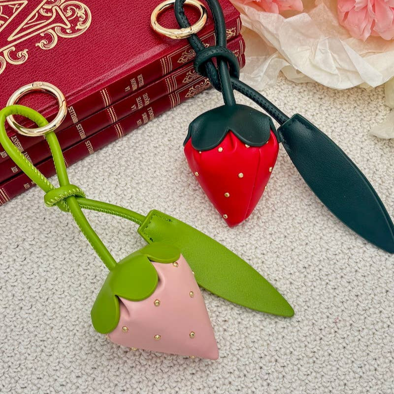 Strawberry-shaped keychain on a textured surface with flowers and a book in the background