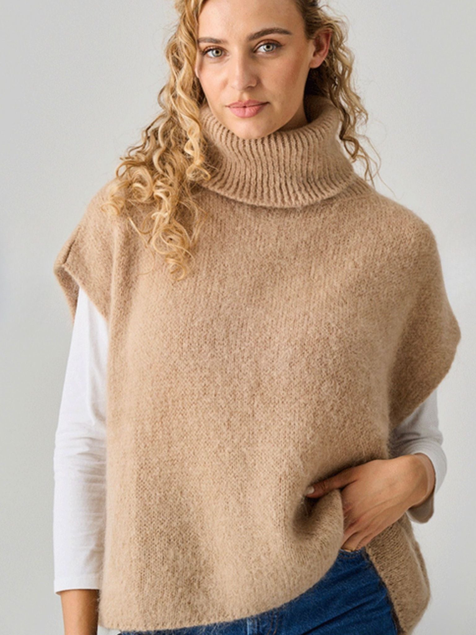 Woman wearing a beige knitted vest over a white shirt with a plain background